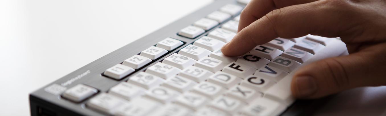 Henkilön käsi tietokoneen näppäimistöllä, jossa on isot kirjaimet.